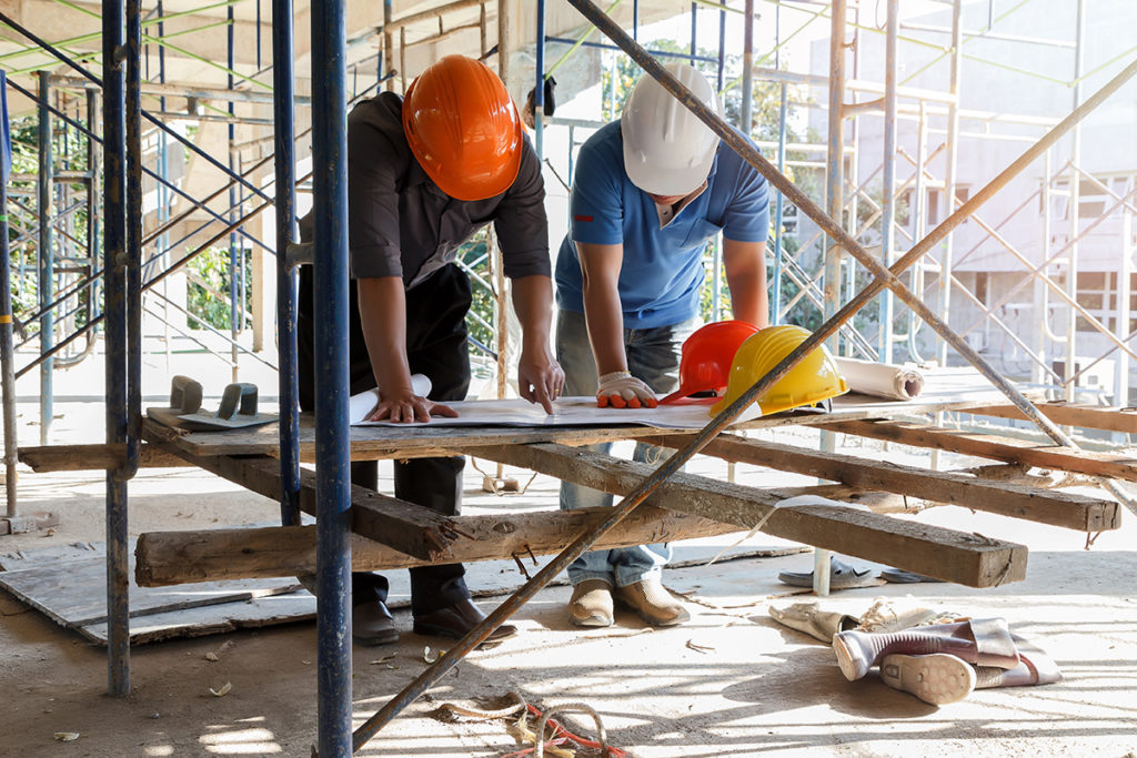 Construction workers reviewing plans amidst scaffolding.